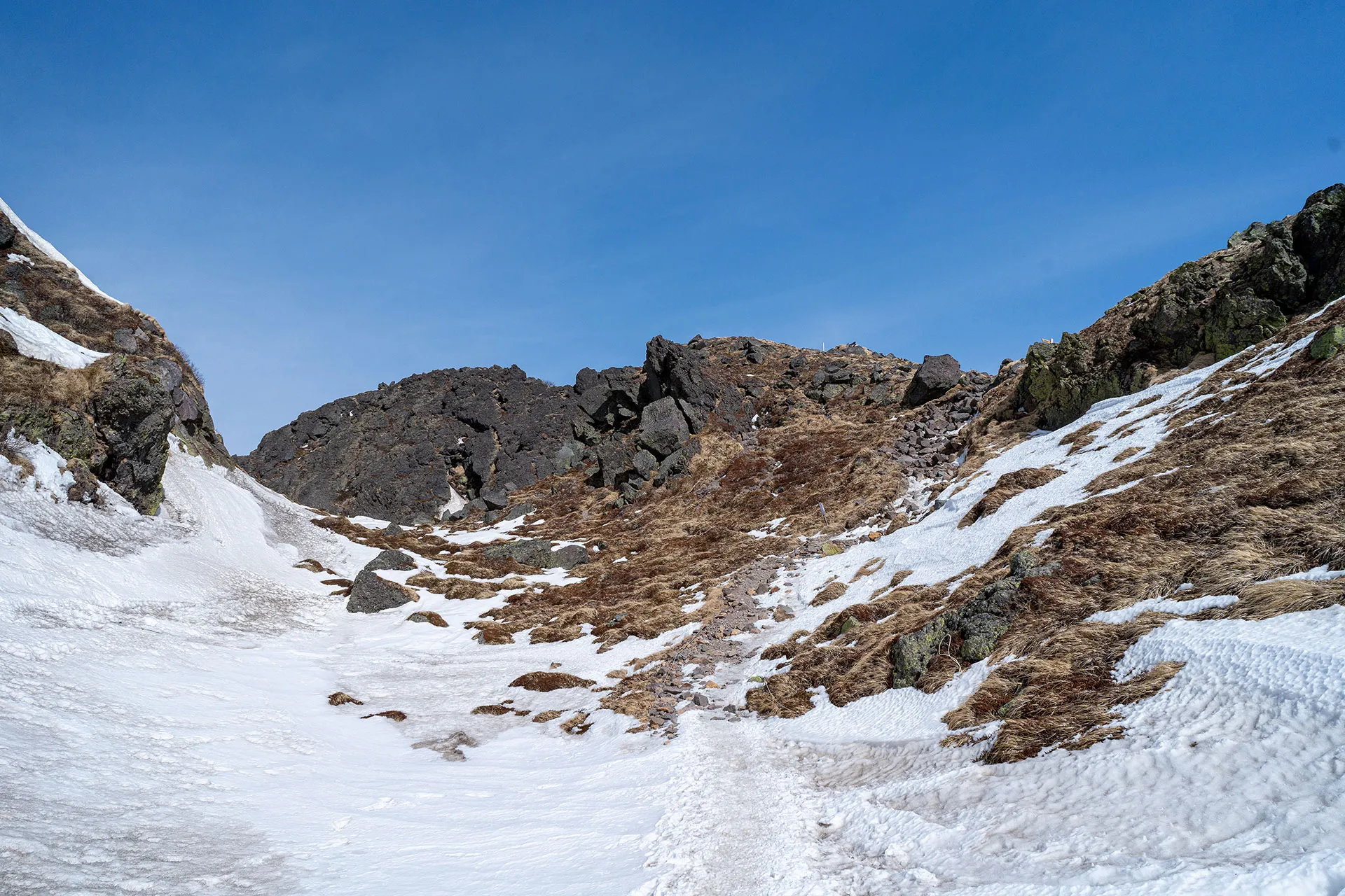 青空の下、岩場と雪が入り混じる日光白根山の登山ルート。アイゼン歩行が必要な本格的な雪山の斜面。
