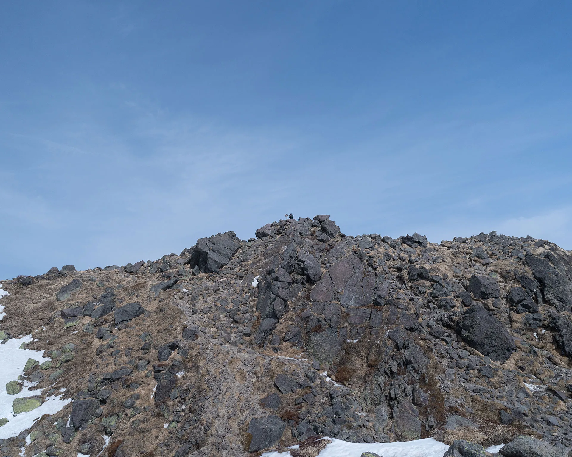 日光白根山の荒々しい岩峰と、その頂に立つ登山者。遮るもののない青空と標高2,500m超の世界。