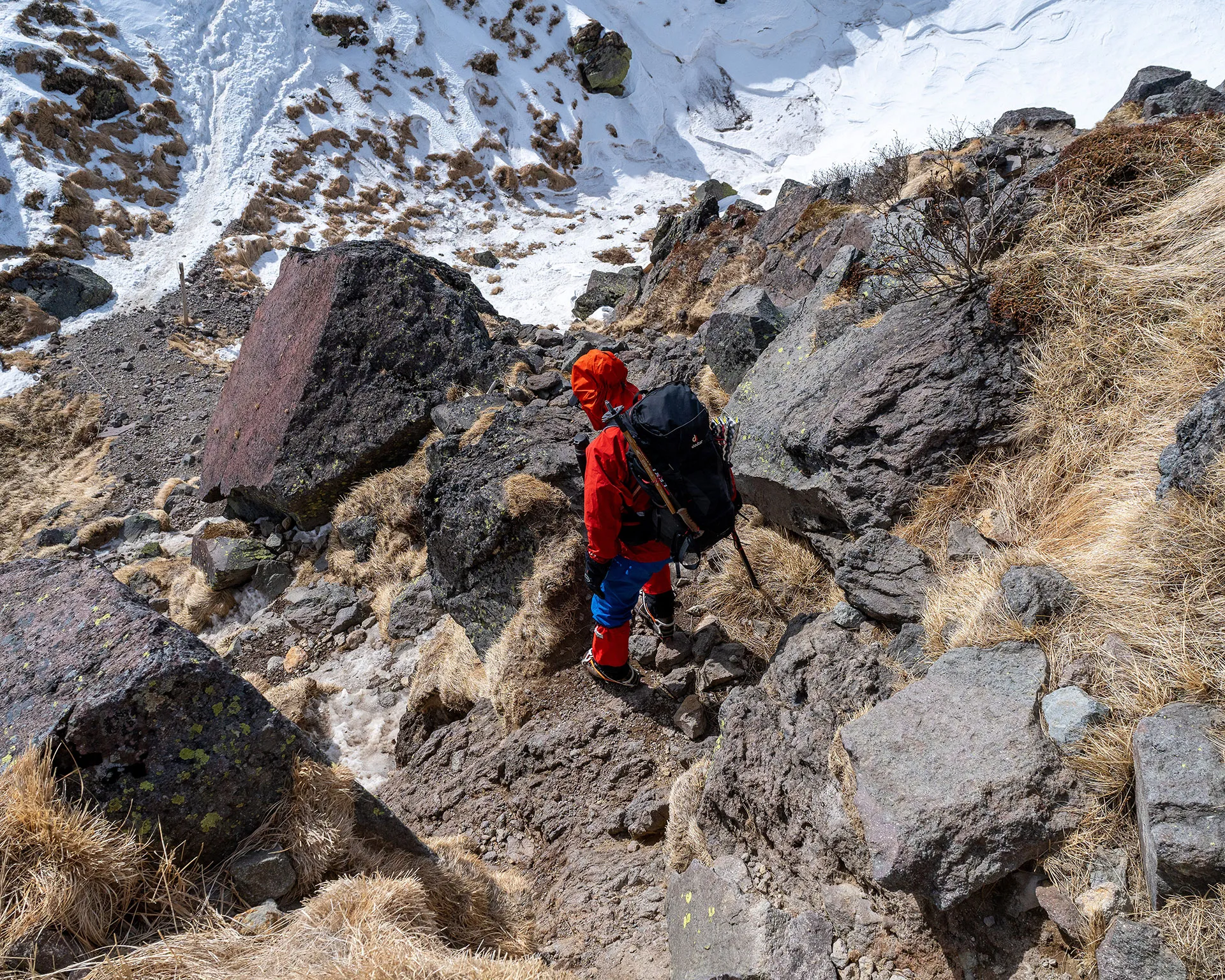 日光白根山の岩場が続く急斜面を慎重に下るハイカー。バックパックを背負い、ピッケルやポールを携えた装備。