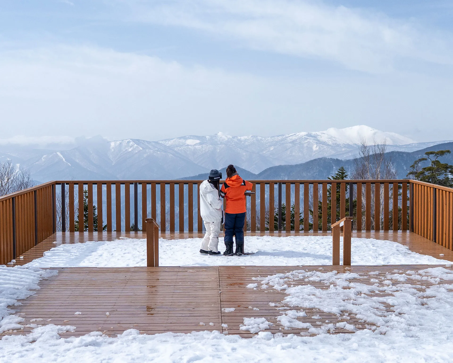 丸沼高原スキー場の展望デッキから、雪化粧をした日光白根山方面を望む観光客。冬の奥日光の山並みを一望する雪上のテラス。