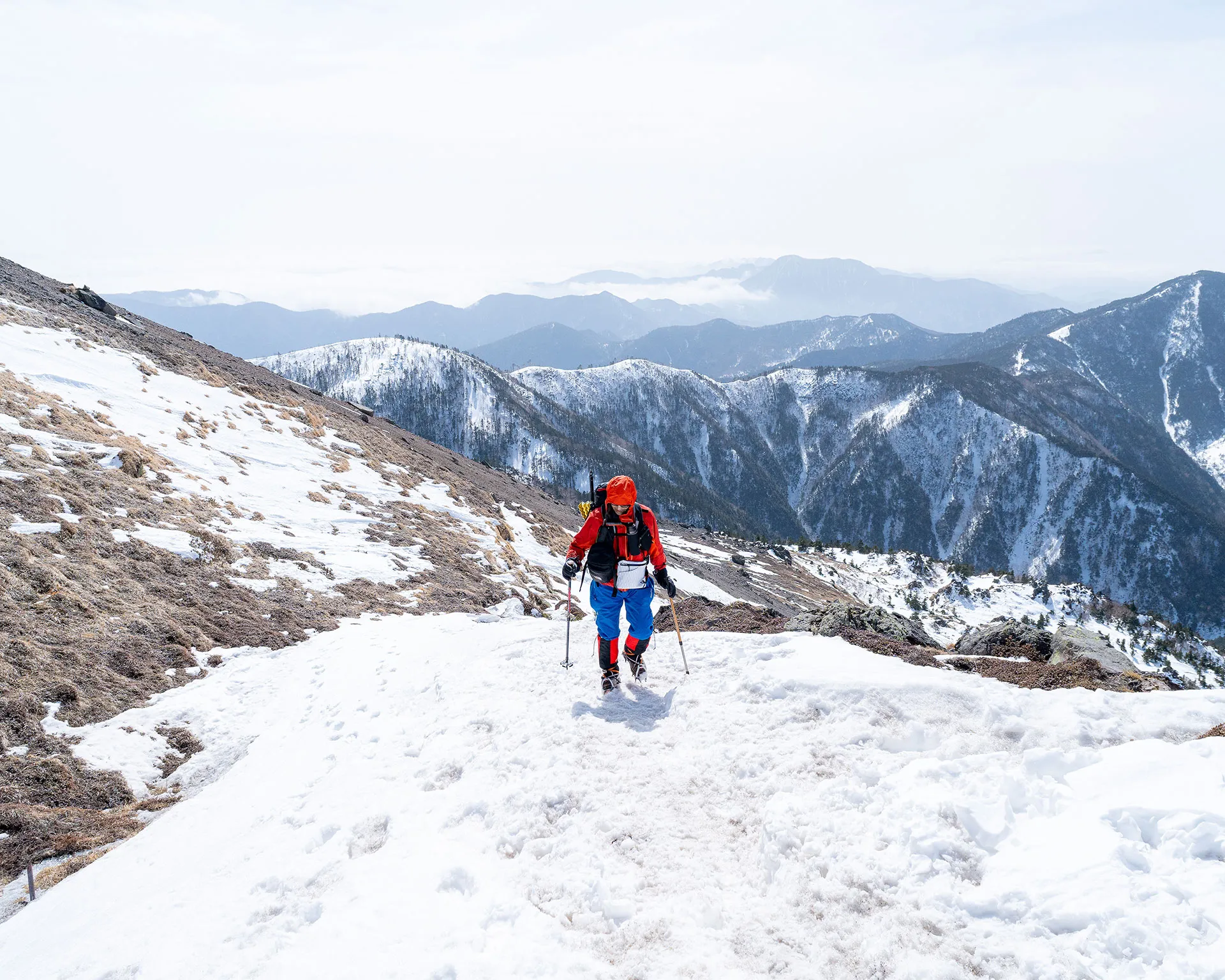 雪に覆われた日光白根山の稜線を歩くハイカー。背景には奥日光の山々と美しい雪景色が広がる。