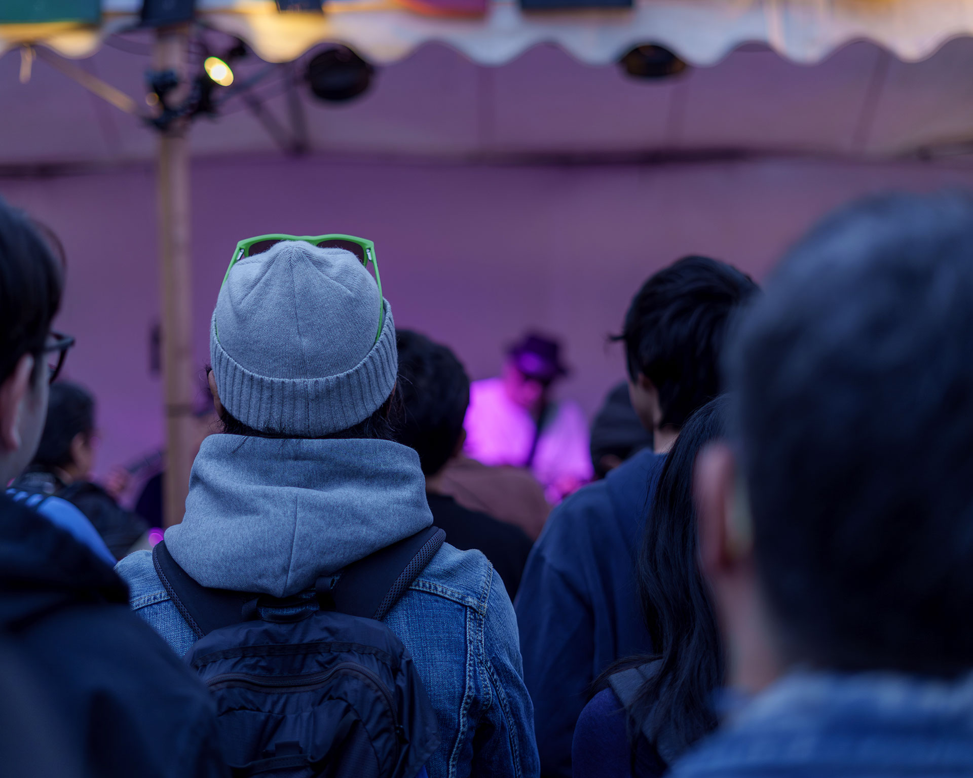 ライブ演奏を静かに見守る観客の後ろ姿。ステージからの照明が夕暮れ時の会場を幻想的に照らす。