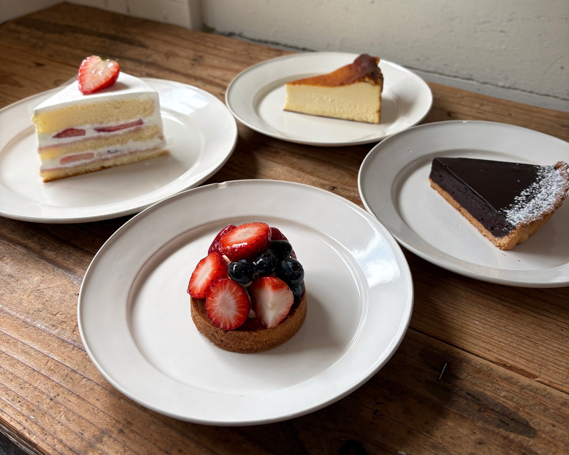 木の卓上に並ぶ、苺ショート・タルト・チョコ・チーズケーキ