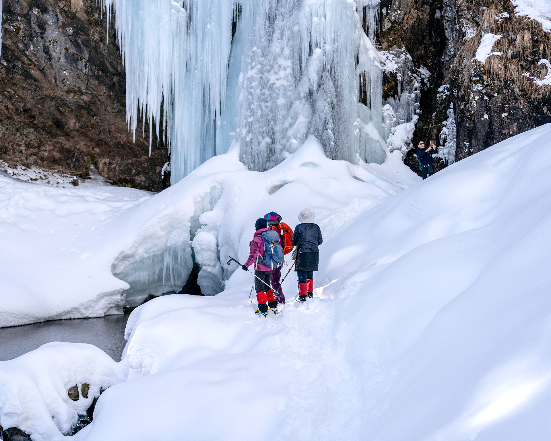 巨大な氷瀑を見上げるハイカー、日光・庵滝のつららと氷柱のクローズアップ、青白い氷の造形美