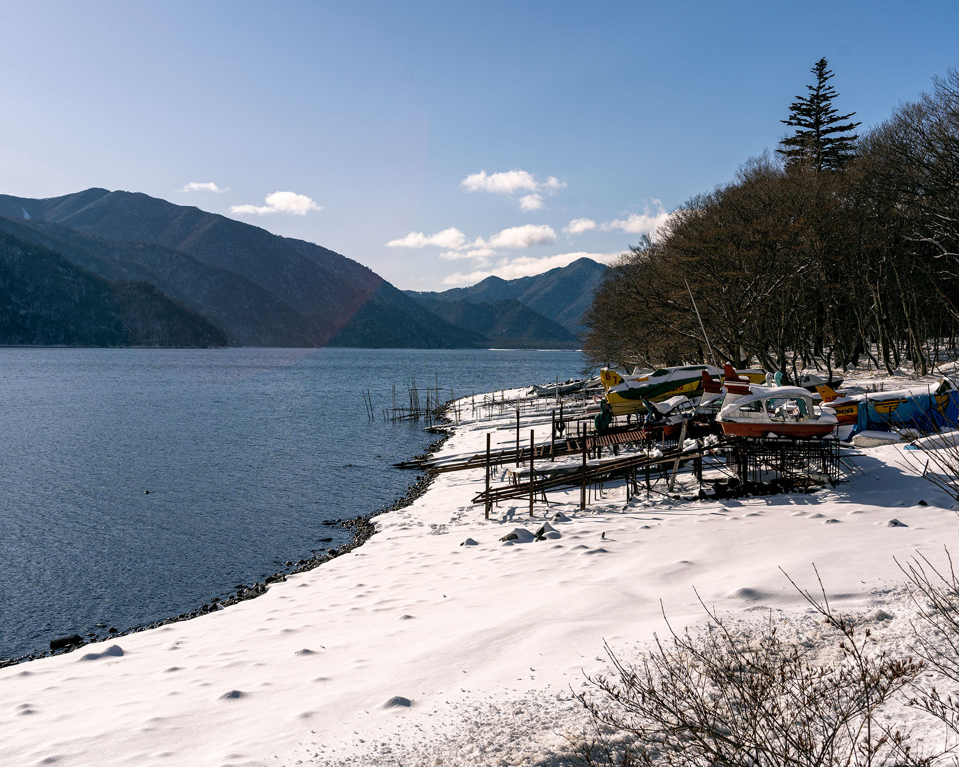 冬の中禅寺湖畔、雪に覆われたボート係留場と静かな湖面、日光の山々を望む冬の湖景色