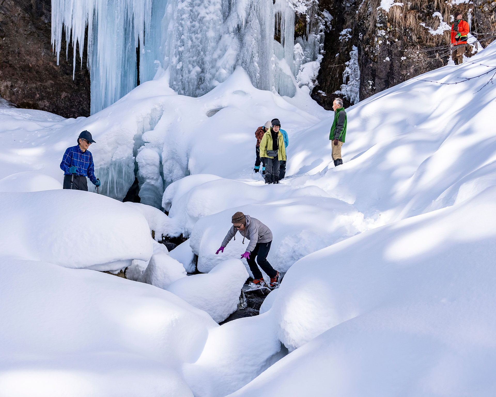 氷瀑を鑑賞するハイカーグループ、庵滝の巨大な氷壁の前で休憩する登山者たち、カラフルな冬山ウェア