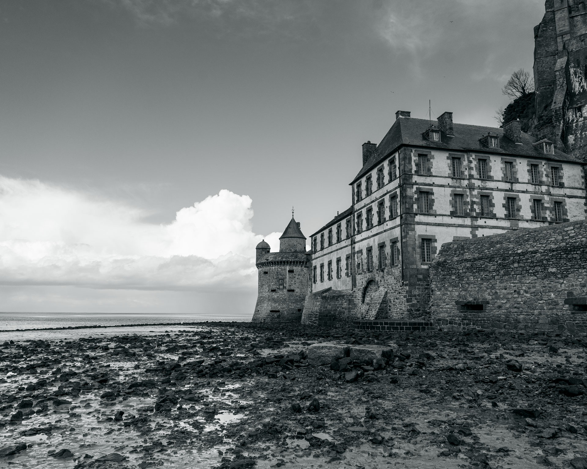 歴史的な要塞城モンサンミッシェル修道院の一部。潮が引いた岩場の海岸線と曇り空が印象的