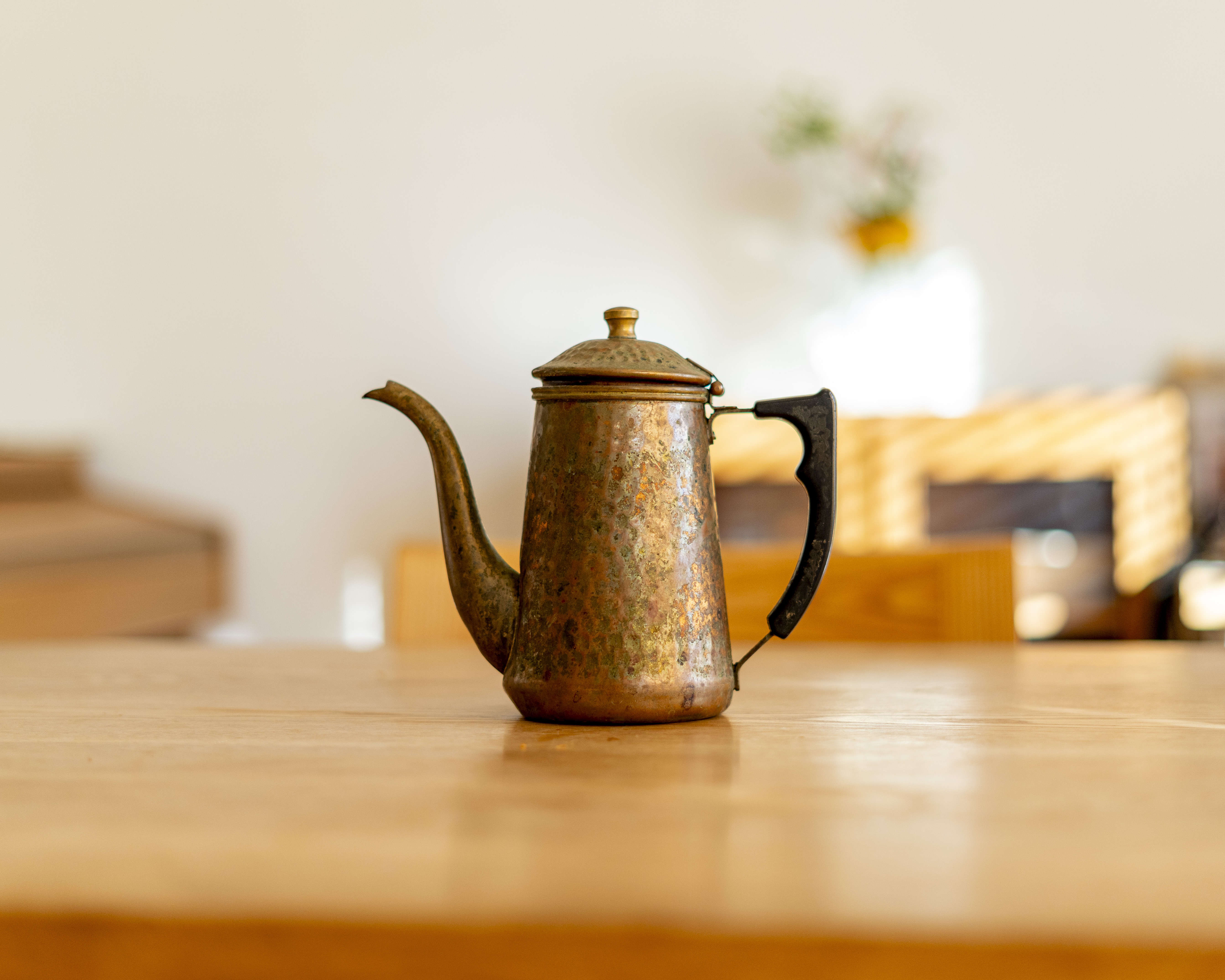 木製テーブルに置かれたアンティークのコーヒーポット「カリタ Cu ケトル 700」。経年の味わいが感じられる真鍮の本体と黒い取っ手が特徴的。