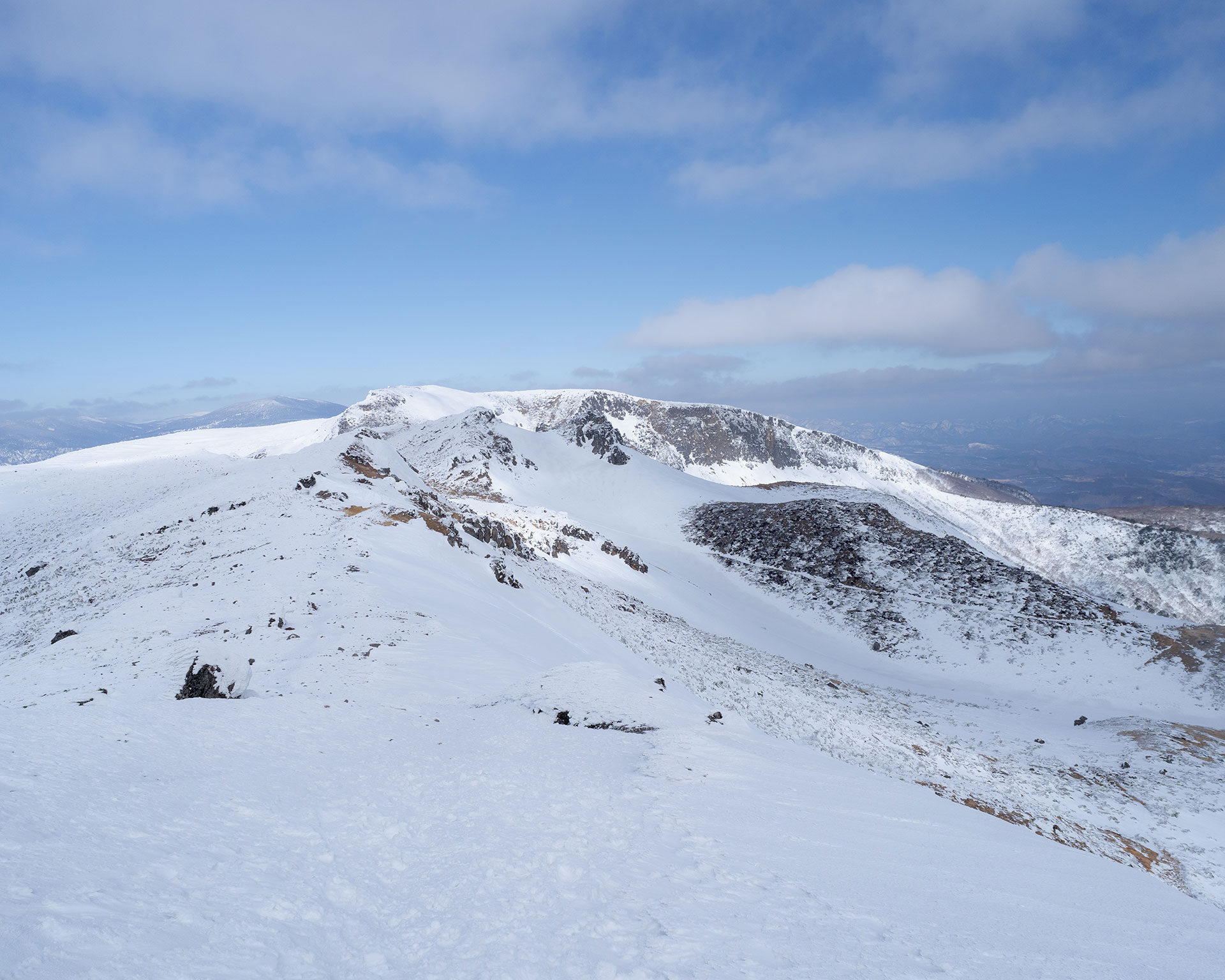 火口を囲む雪の稜線、中央に火口湖が広がる