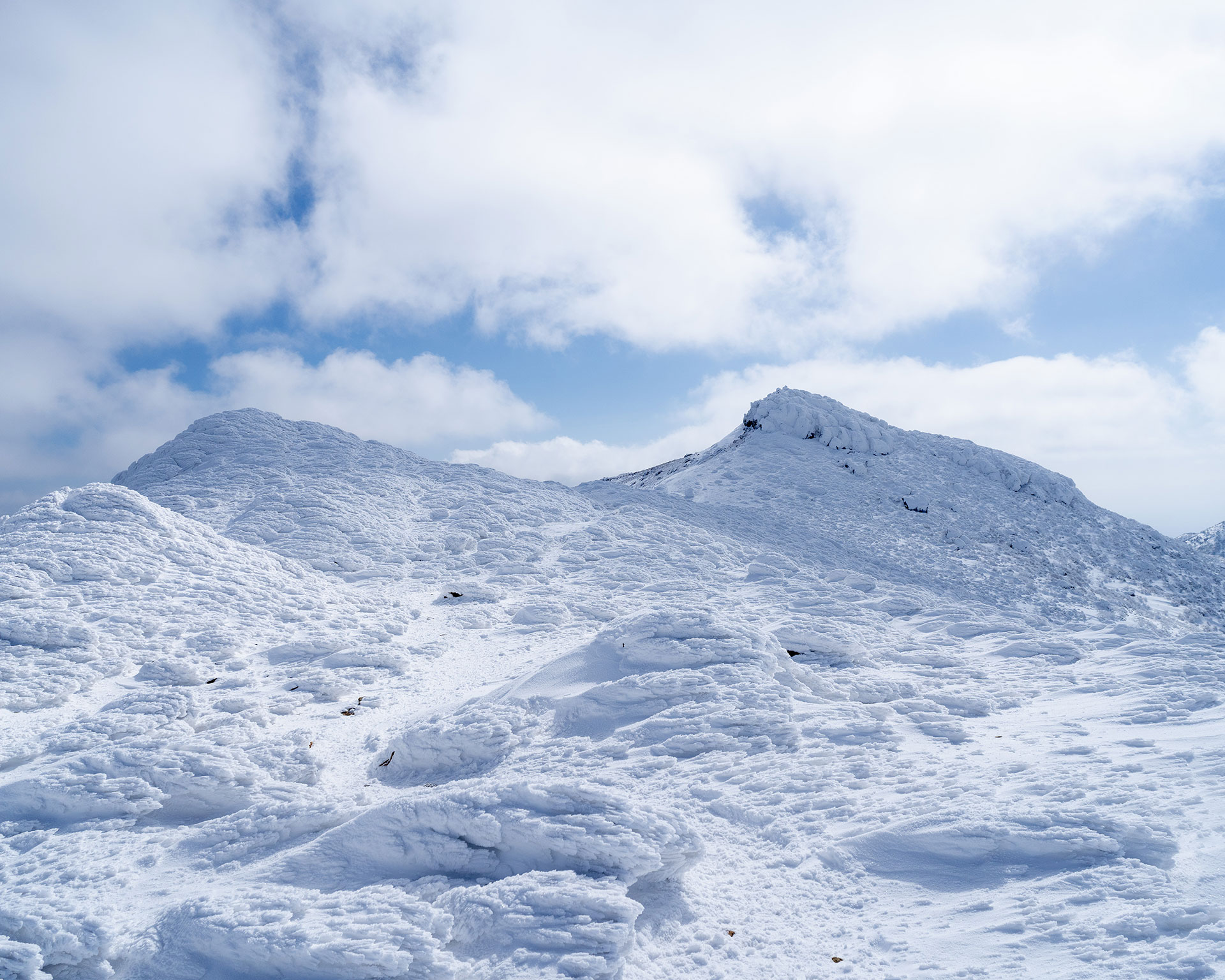 雪と氷に覆われた山頂付近、波状の雪面が広がる