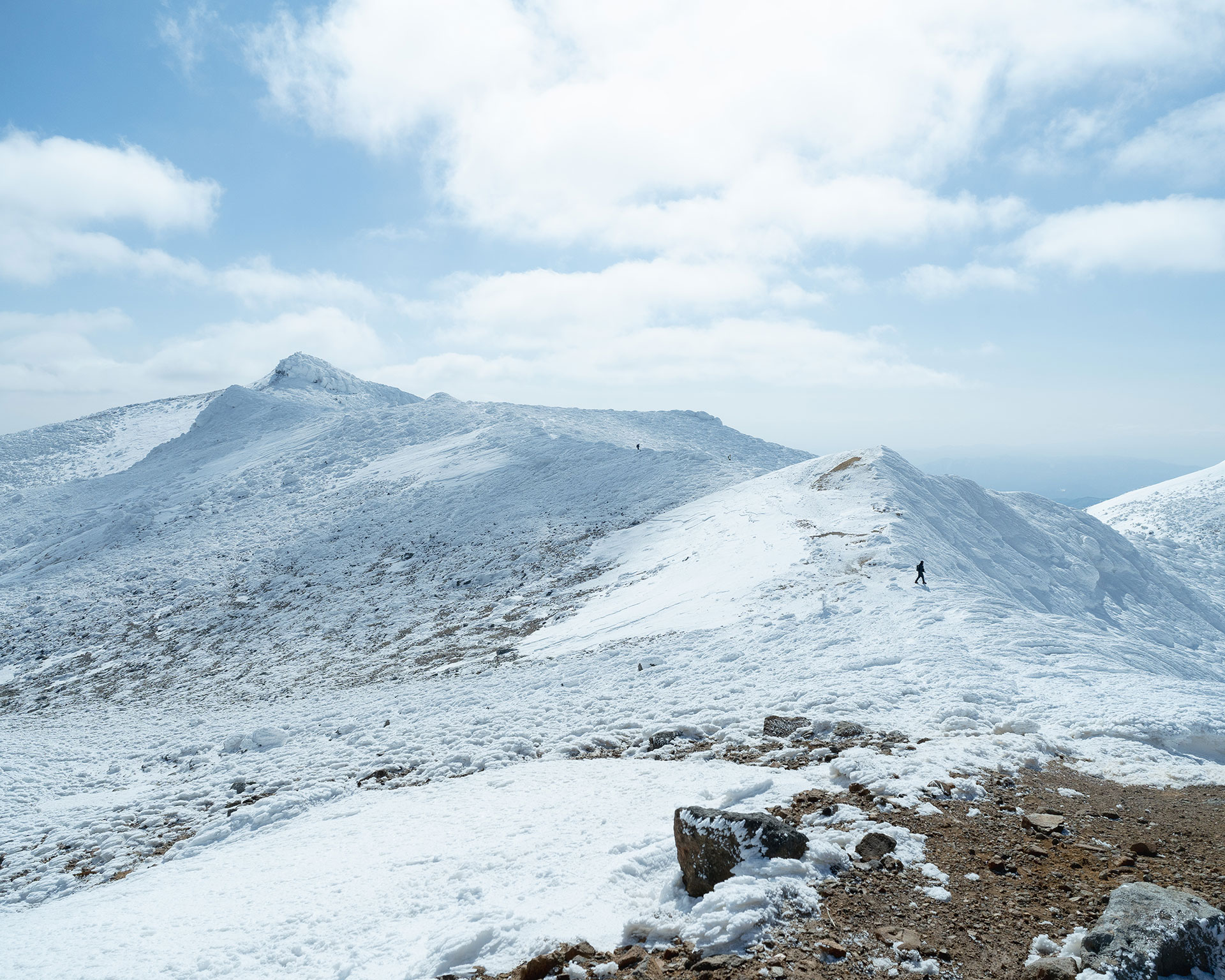 雪の稜線を歩く登山者、手前に岩が点在
