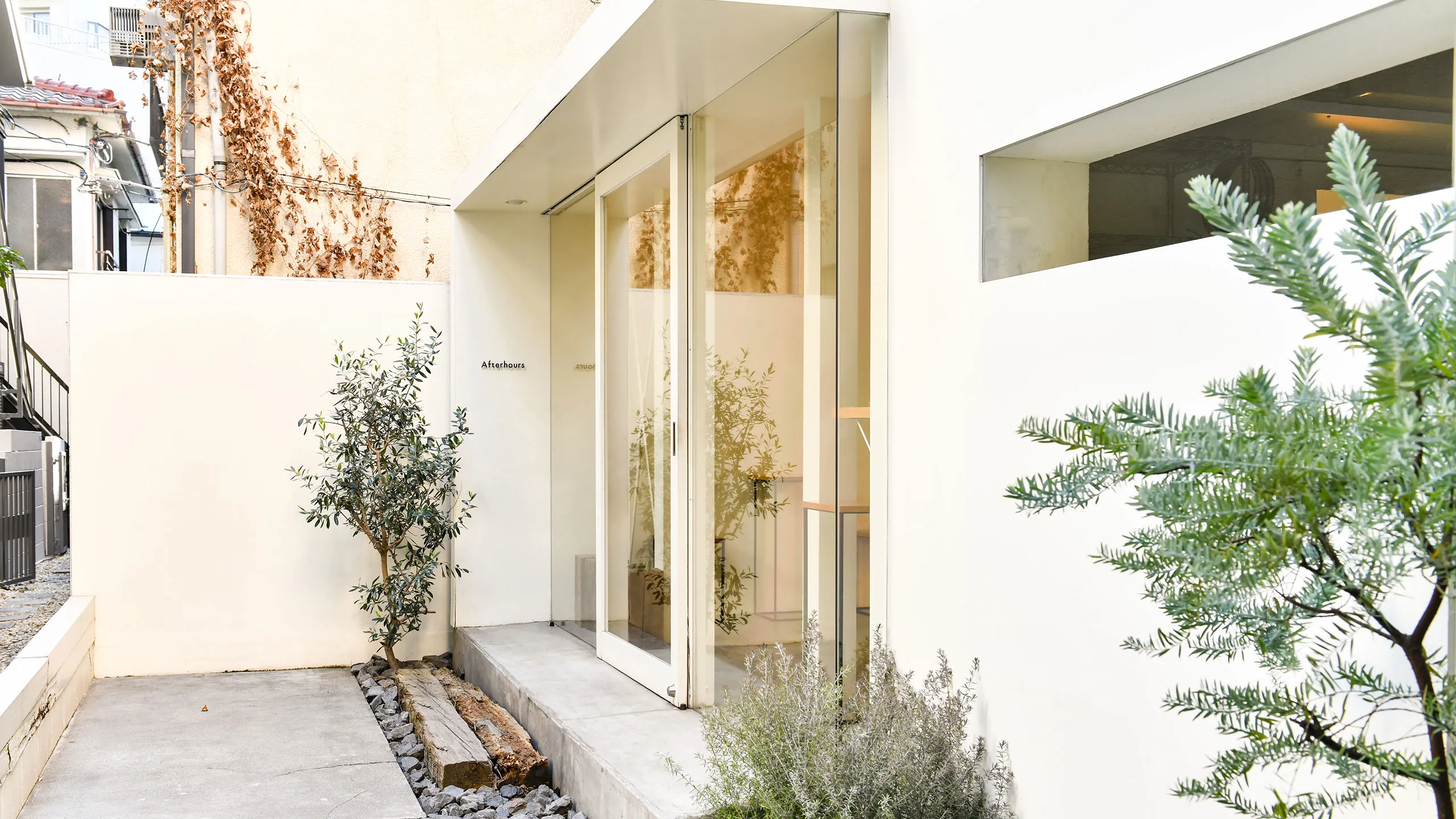推奨：SEO特化型altテキスト
代々木公園近くのケーキ店Afterhours（アフターアワーズ）の店舗外観。白壁とガラス扉、オリーブの木が調和したミニマルな入り口
