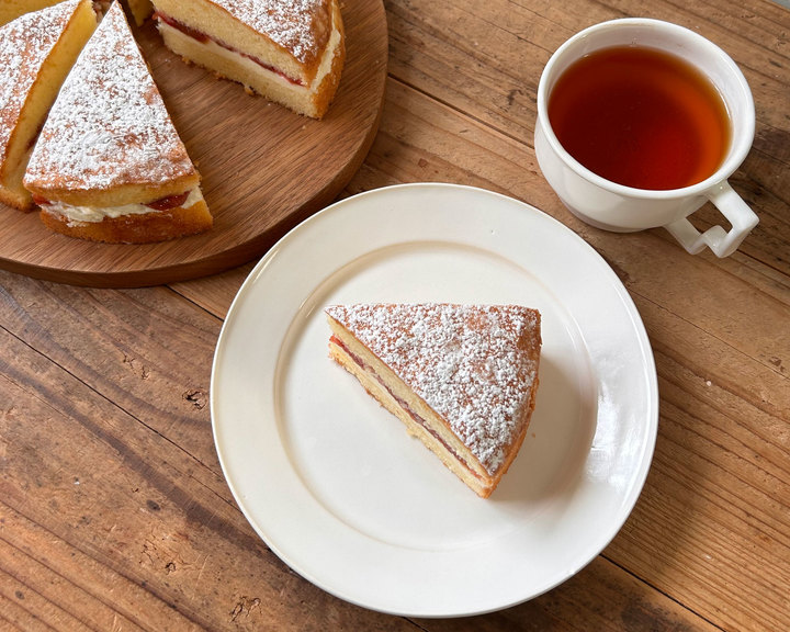 木製テーブルに置かれたジャム入りスポンジケーキと紅茶のティータイムセット