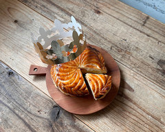 ガレット・デ・ロワ（アーモンドクリームのパイ菓子）と紙の王冠。カットされた断面と艶やかなパイ生地の質感がわかる商品写真。