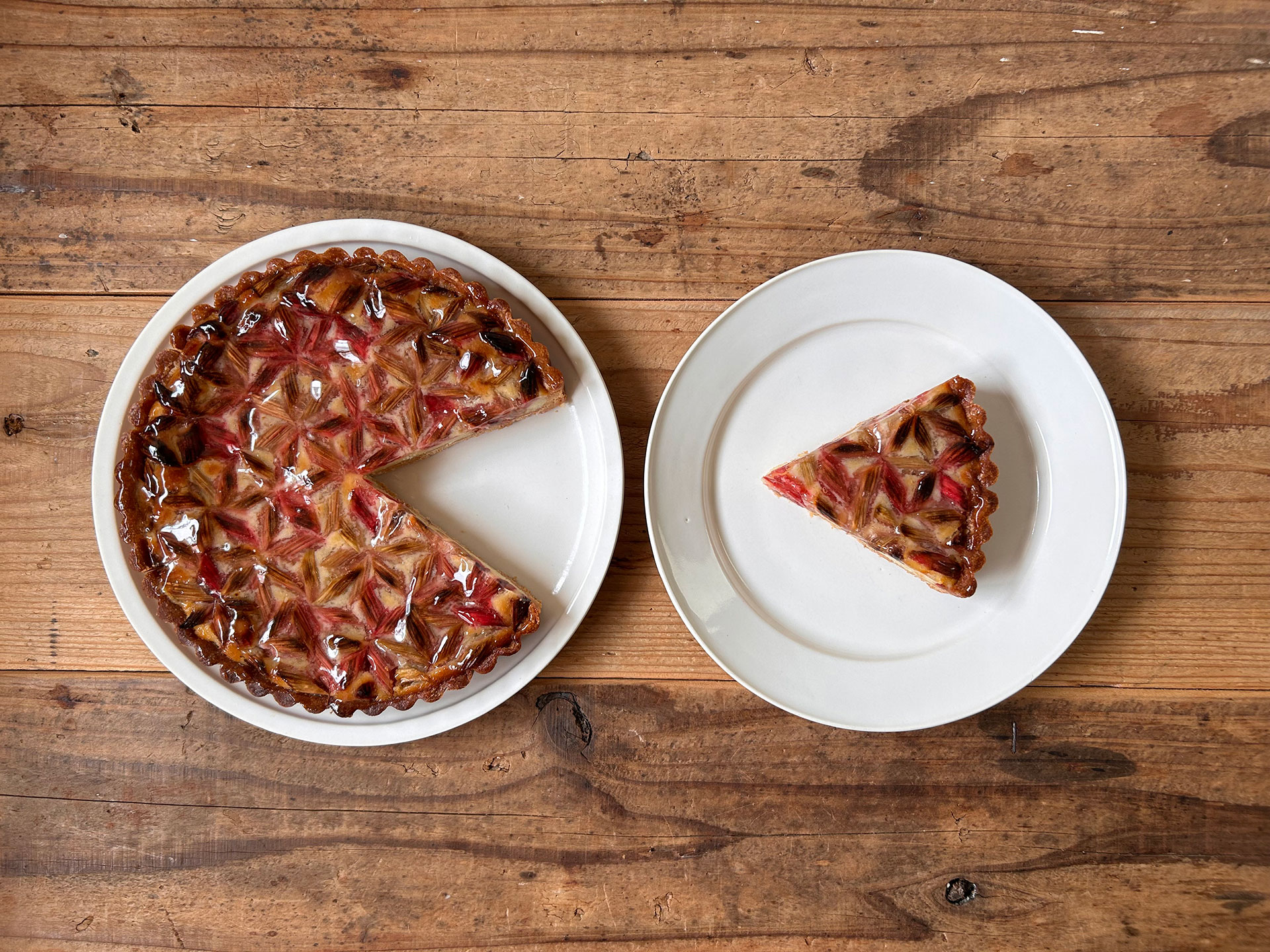 木のテーブルに置かれた赤いルバーブのタルト。一切れカットされ、白い皿に盛り付けられている。