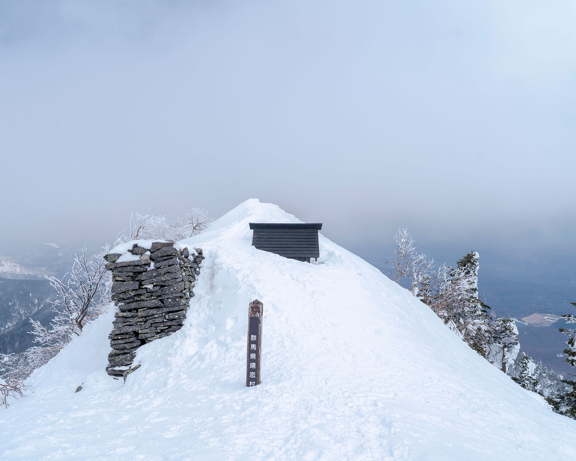 四阿山頂上の雪に埋もれた山小屋と石碑、日本語の標識が立つ雪深い頂上エリア