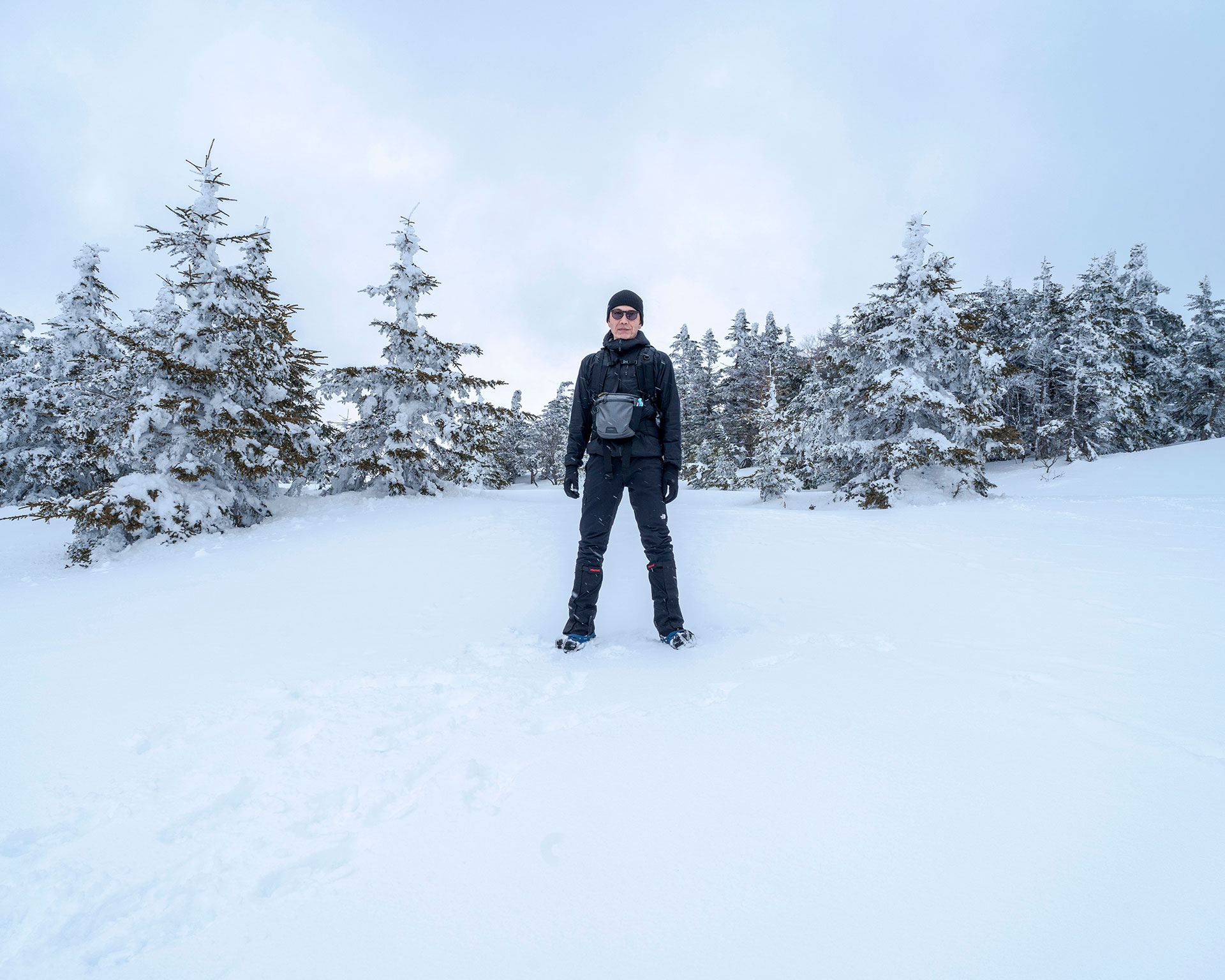 四阿山の雪景色の中たたずむ登山者、冬の針葉樹林に囲まれた雪のトレイル